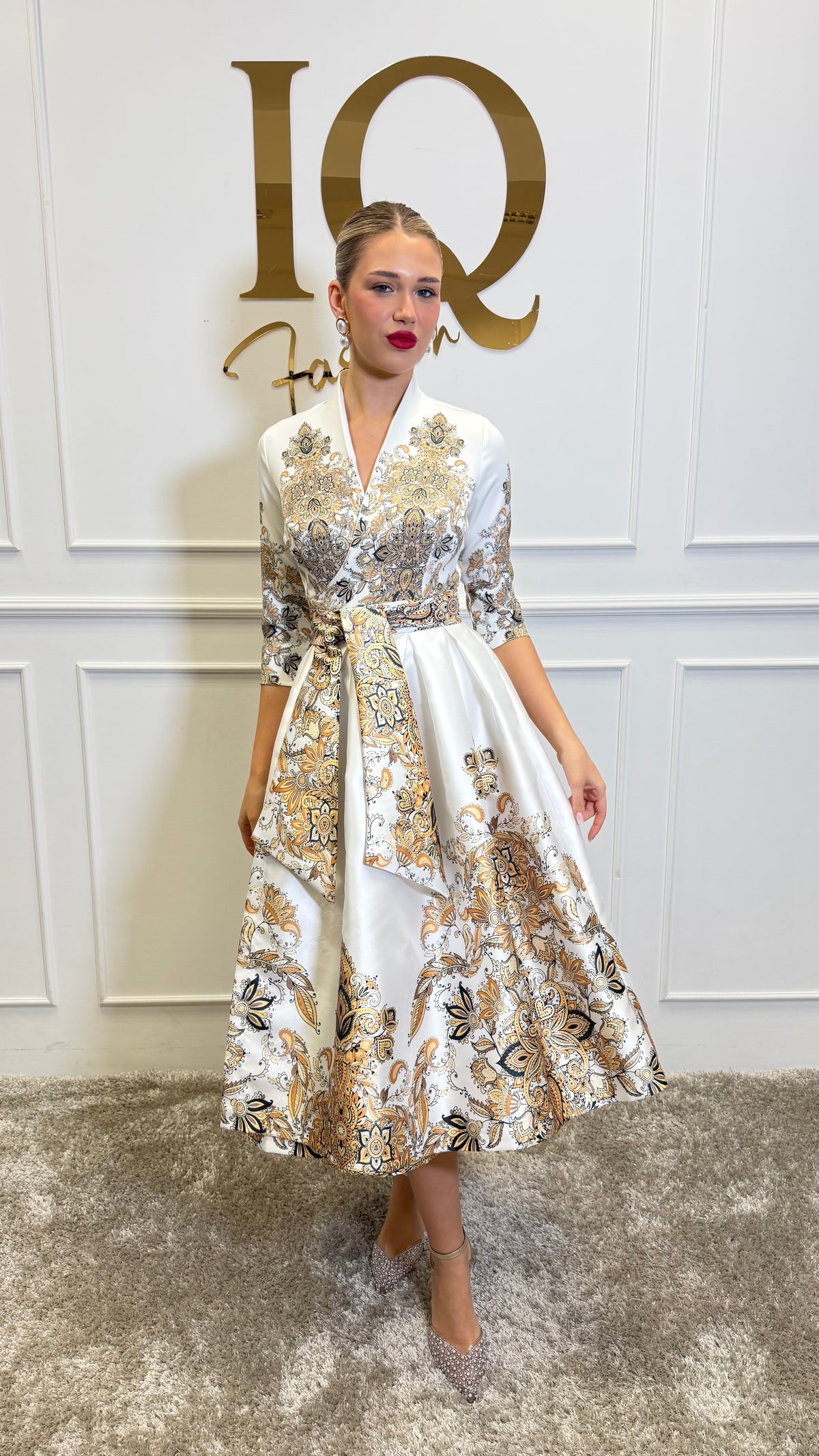 Rochie Goldie White de la iqfashioncluj, rochie elegantă albă cu detalii aurii, purtată pe model într-un decor neutru.